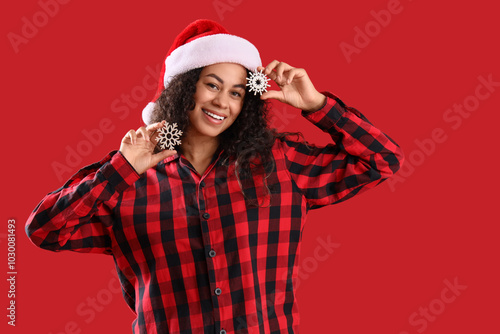 Pretty young African-American woman with Christmas snowflakes on red background