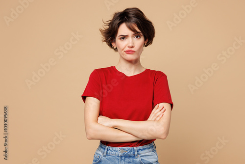 Young frowning grumpy upset dissatisfied sad woman she wear red t-shirt casual clothes hold hands crossed folded look camera isolated on plain pastel light beige background studio. Lifestyle concept. photo