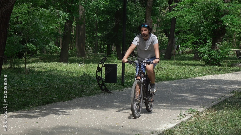 Man cycling on a paved path in a lush green forest on a sunny day. Man cycling on a paved path in a lush green forest on a sunny day.