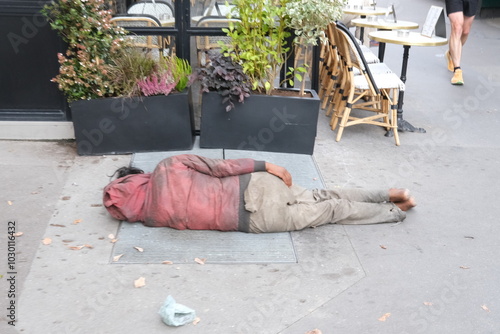 Fototapeta Naklejka Na Ścianę i Meble -  A man sleeping in the street near a Parisian cafe. Paris, France - October 3, 2024. 