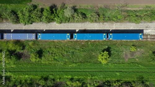 Aerial view of a freight train traveling with cargo carriages between cultivated plots