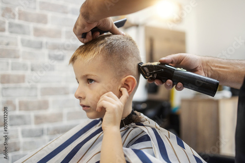 Photography Portrait of a cute little blond boy sitting in chair at barber shop and getting a new haircut