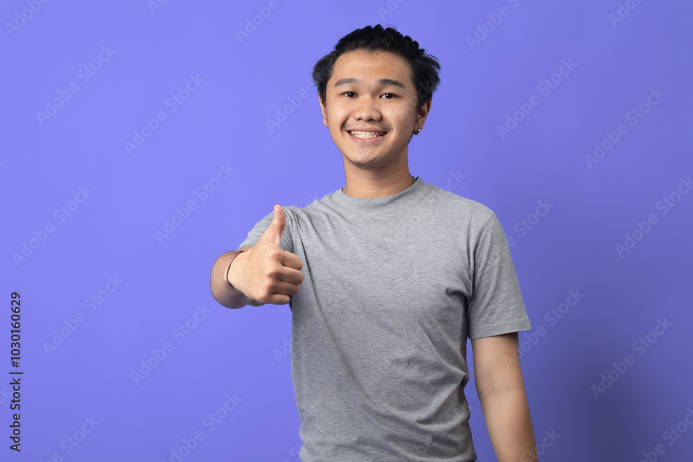 An Asian man giving a thumbs-up with a friendly smile, standing in front of a purple background. He is wearing a gray t-shirt with a circular graphic on the chest, exuding positivity and confidence An Asian man giving a thumbs-up with a friendly smile, standing in front of a purple background. He is wearing a gray t-shirt with a circular graphic on the chest, exuding positivity and confidence