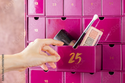 Advent calendar, boxes with numbers with decorative cosmetics for makeup gift and hand reaching for it, closeup. Waiting, Christmas countdown.