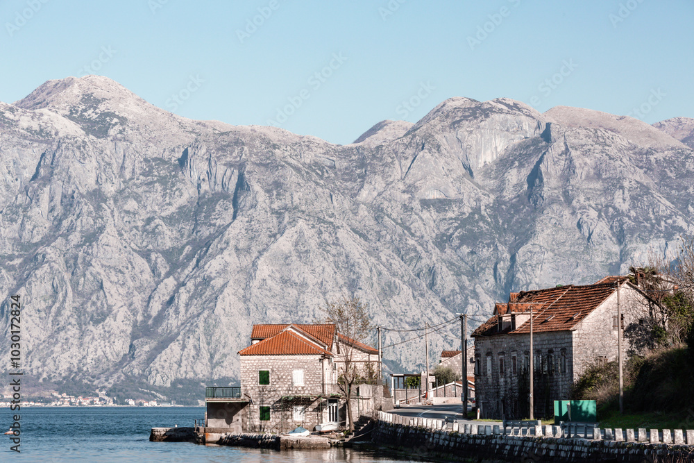 Fototapeta premium Bay of Kotor, Montenegro. Stone houses by the waterfront with red-tiled roofs, set against a backdrop of rugged mountains