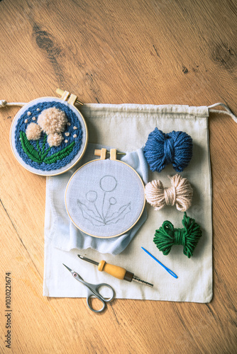 Flatlay of two embroidery hoops with funiched and unfinished projects, balls of yarn, scissors and punch needle.