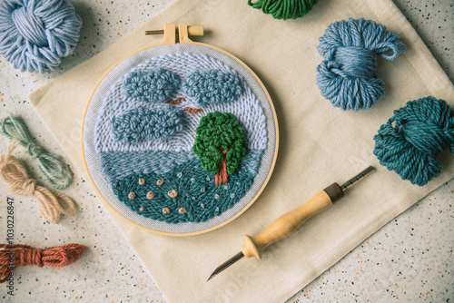 Embroidery in a hoop with a big punch needle on the side and several skeins of yarn.