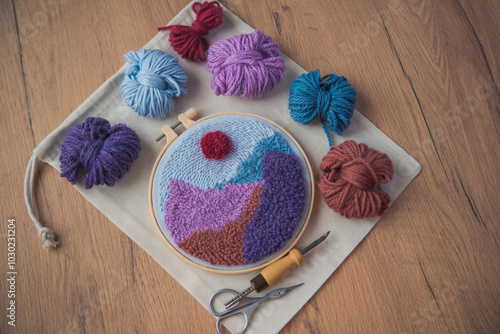 Embroidered mountains in a round frame with skeins os wool, punch needle and scissors around.
