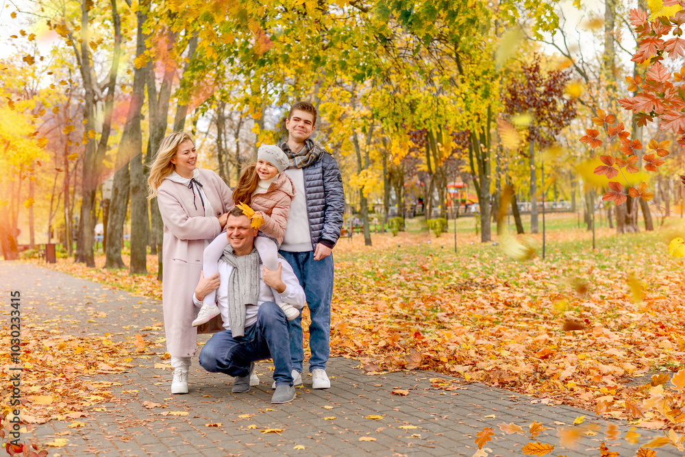 Fototapeta premium Banner with a Happy family in the autumn park: mom, dad, little daughter, teenage son. Background: yellow trees and foliage. Family vacation concept