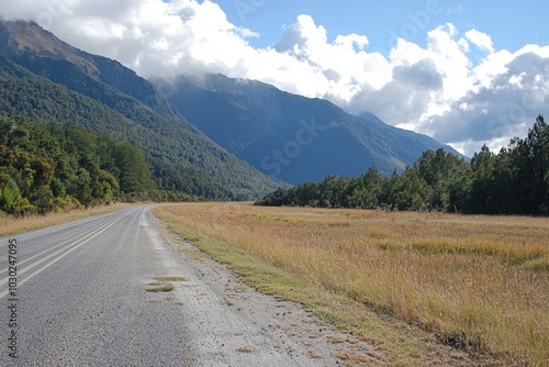 A serene gravel road winding through lush mountains and golden fields under a bright sky