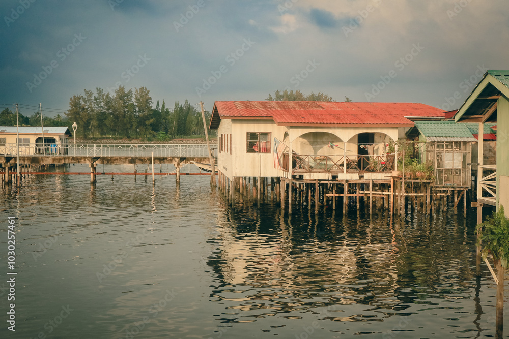 Obraz premium Houses on stilts reflect in the calm waters of Kota Kinabalu during a peaceful afternoon