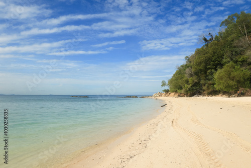 Beautiful sandy beach on Mamutik Island, Malaysia, under a clear blue sky with gentle waves lapping at the shore in the afternoon sun