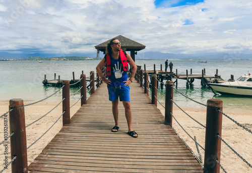 A tourist enjoys a day by the beach in Malaysia, posing confidently on a wooden pier surrounded by calm waters and boats photo