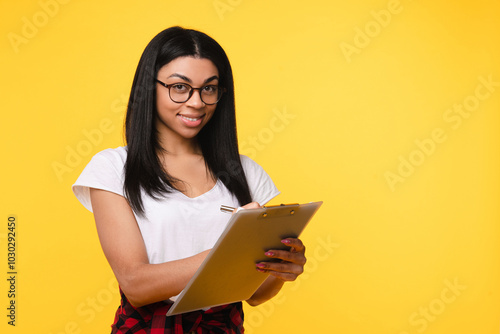 Portrait of attractive cheerful african woman female student manager girl holding clipboard signing paper copy space isolated over bright yellow color background copy free space