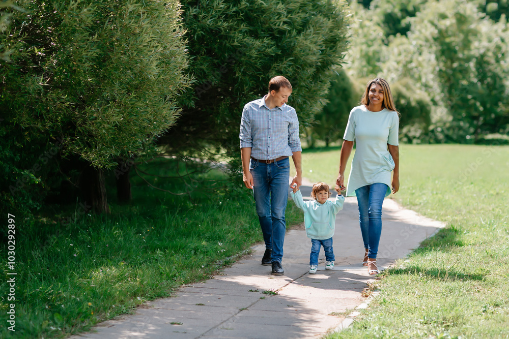Multi-ethnic, African-American and European family walking down the road holding hands. Black baby, mother, father together in the park. Multi-ethnic, African-American and European family walking down the road holding hands. Black baby, mother, father together in the park.