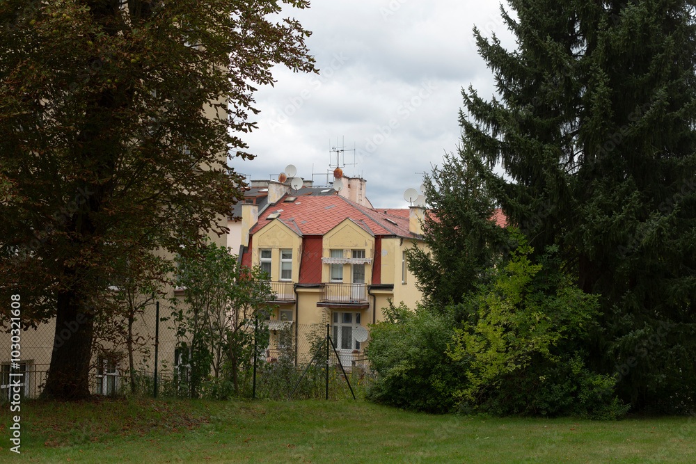 A very large yellow house featuring a bright red roof is beautifully surrounded by lush green trees and soft grass all around it A very large yellow house featuring a bright red roof is beautifully surrounded by lush green trees and soft grass all around it