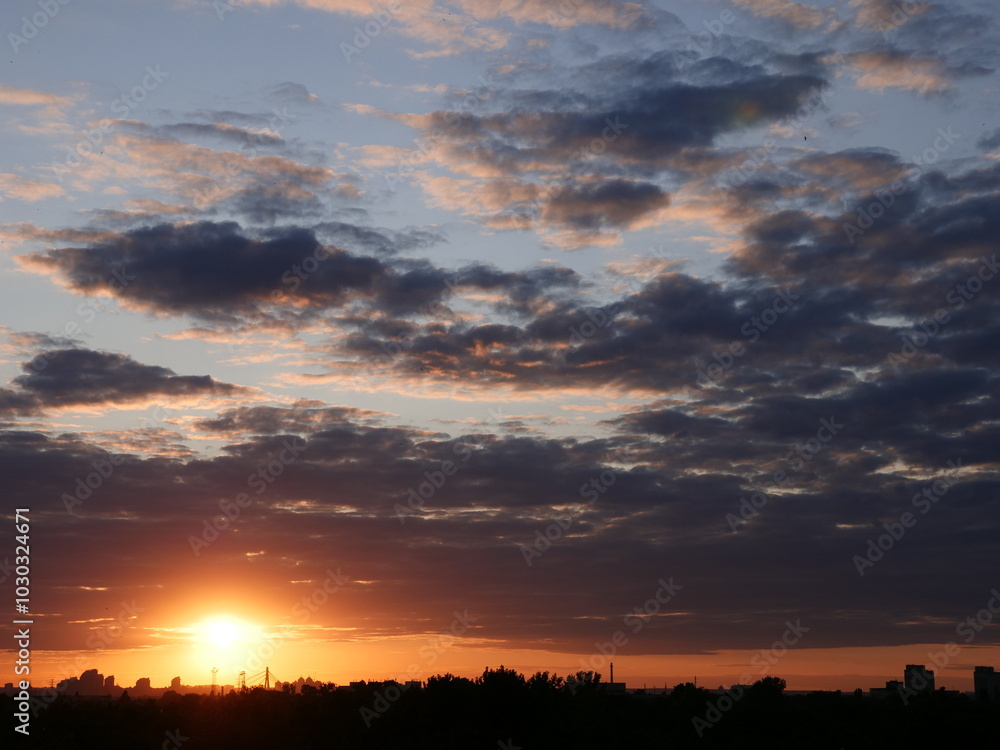Amazing orange sunset over Kyiv (Kiev) city with building silhouettes. Industrial cityscape of black buildings against the backdrop of glowing orb of the setting sun and red and lilac scenic clouds.