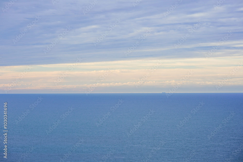 A calm blue sea stretches toward the horizon under a soft sky with layers of clouds A calm blue sea stretches toward the horizon under a soft sky with layers of clouds