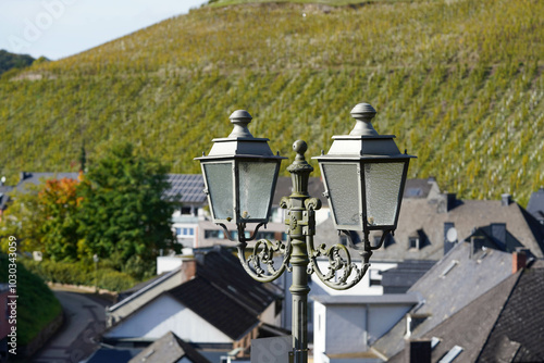 Im Vordergrund steht ein klassischer Laternenpfahl mit Häuserhintergrund und einem Weinberg photo