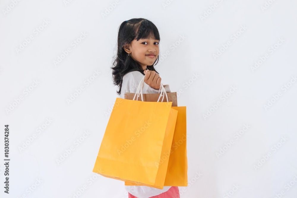 Portrait a little Asian girl holding yellow and brown paper shopping bags on a white background Portrait a little Asian girl holding yellow and brown paper shopping bags on a white background