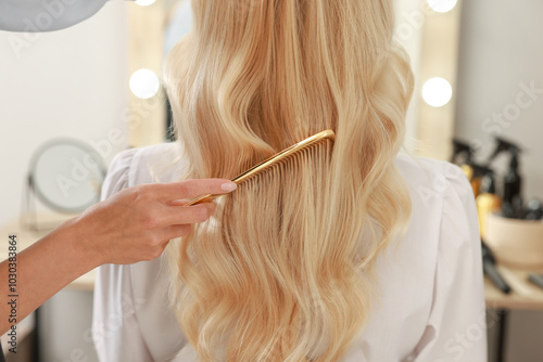 Professional hairdresser combing woman's hair in salon, closeup photo