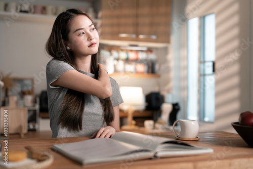 Young woman massaging her neck, indicating discomfort or strain while working on a laptop at home