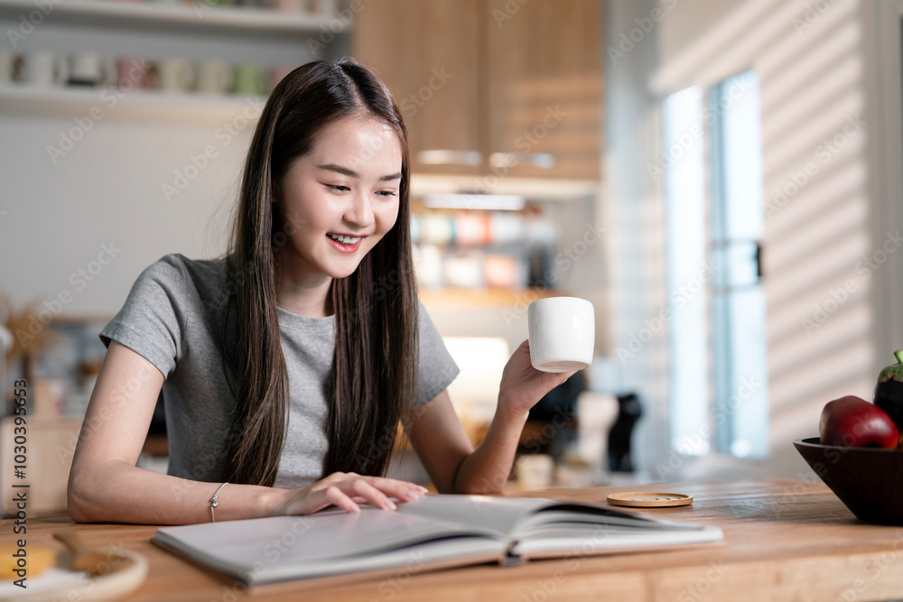 Young woman reading book and drinking coffee or cocoa at home. Beautiful female with cup of tea passionate about reading exciting novel while sitting in kitchen room at home Young woman reading book and drinking coffee or cocoa at home. Beautiful female with cup of tea passionate about reading exciting novel while sitting in kitchen room at home