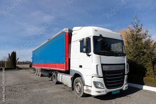 Commercial vehicle for business transportation. Semi-trailer tractor with a white cab and a long blue trailer. ten wheeler truck parked on a sunny day against the sky, front and side view.