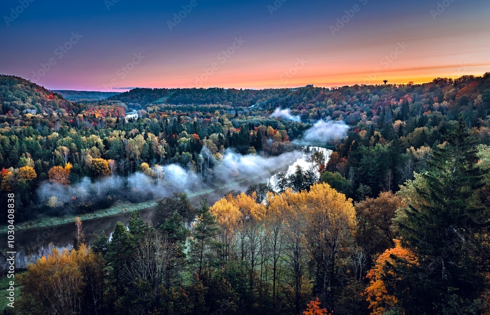 Colorful sunrise over the Gauja National park valley. Sigulda city panorama from drone with forest in autumn colors.