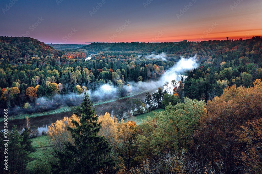 Colorful sunrise over the Gauja National park valley. Sigulda city panorama from drone with forest in autumn colors.