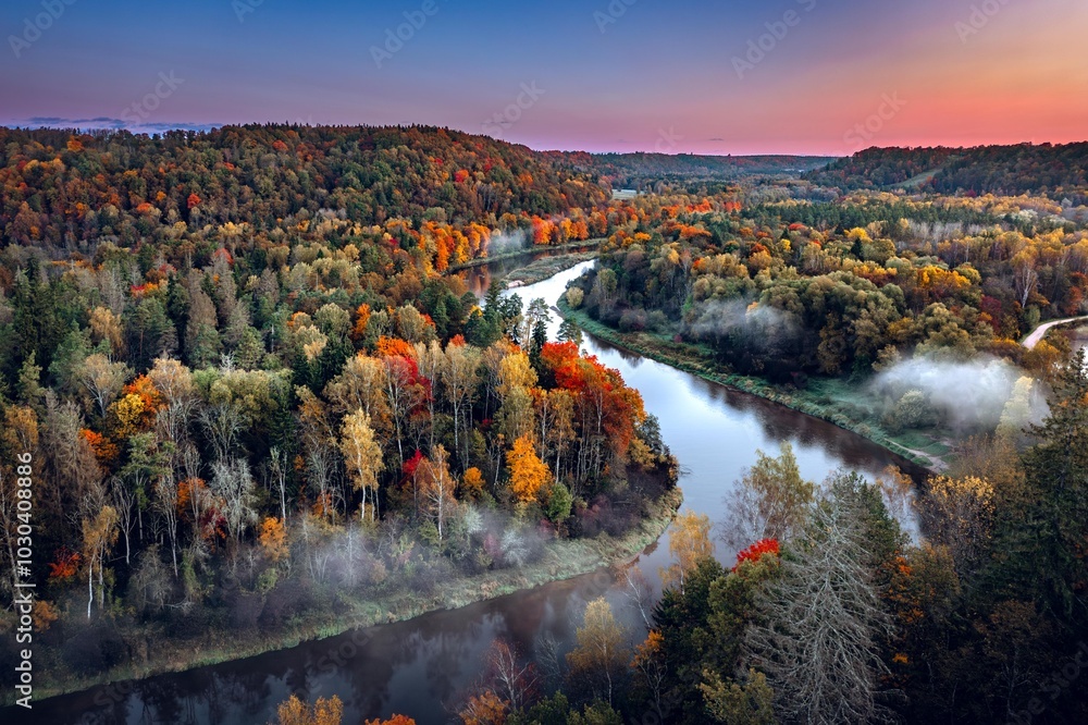 Colorful sunrise over the Gauja National park valley. Sigulda city panorama from drone with forest in autumn colors.