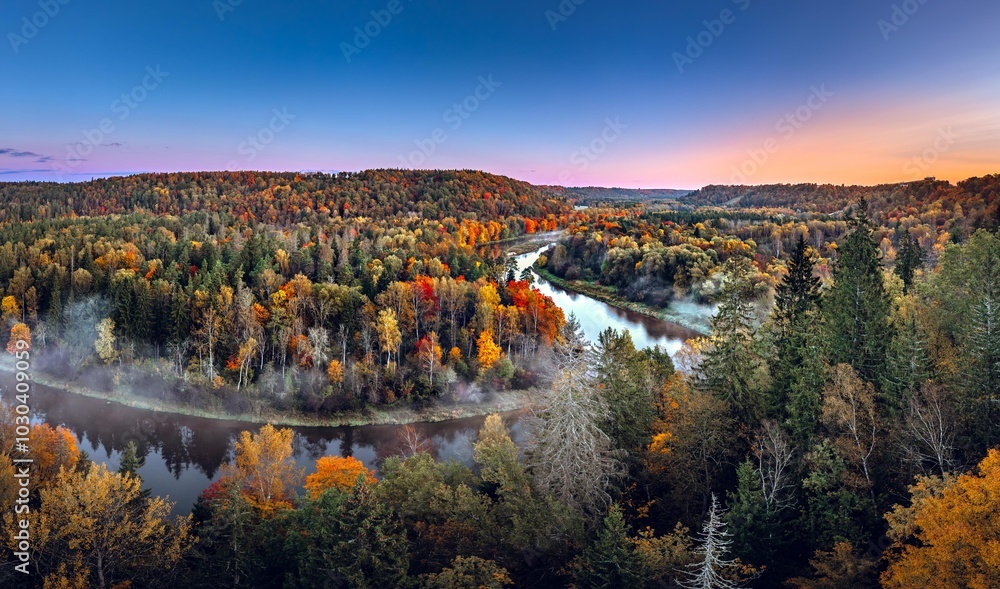Colorful sunrise over the Gauja National park valley. Sigulda city panorama from drone with forest in autumn colors.