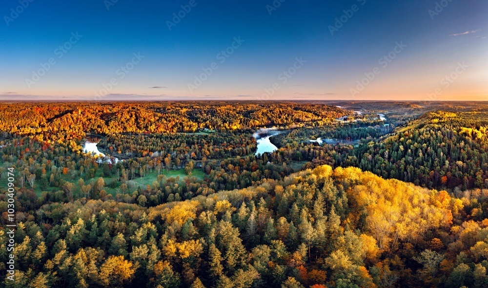 Colorful sunrise over the Gauja National park valley. Sigulda city panorama from drone with forest in autumn colors.