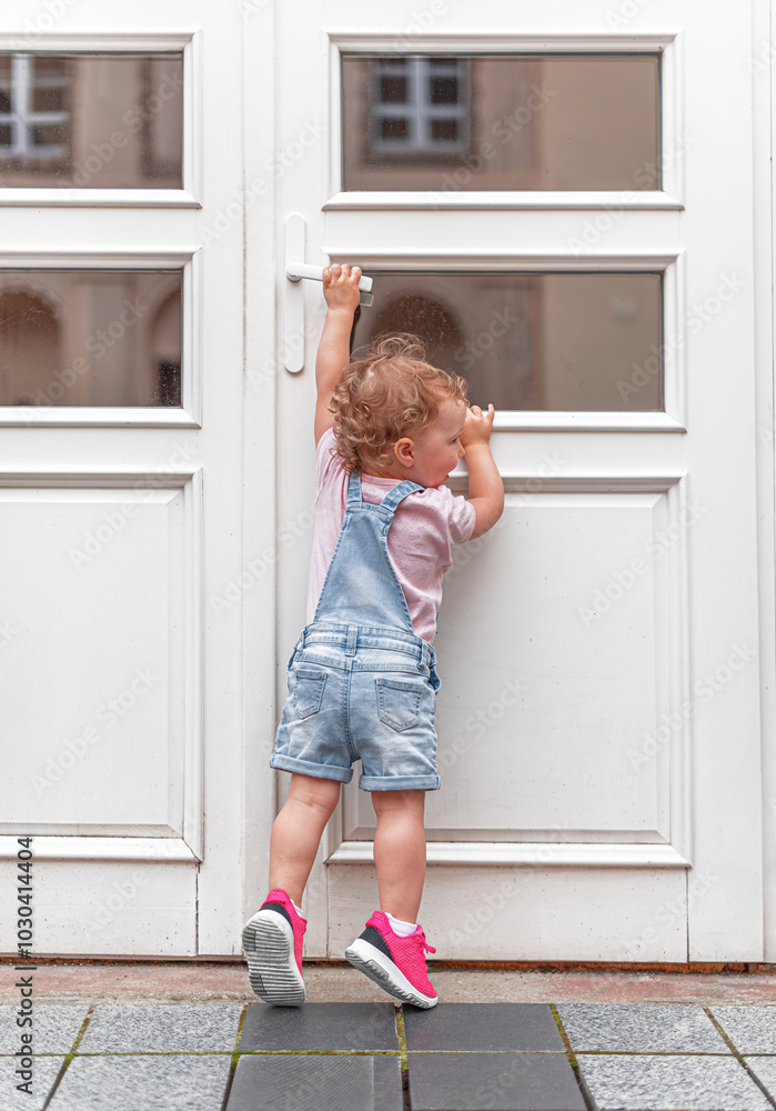 The child tries to open the door. The child reaches for the doorknob on the street.