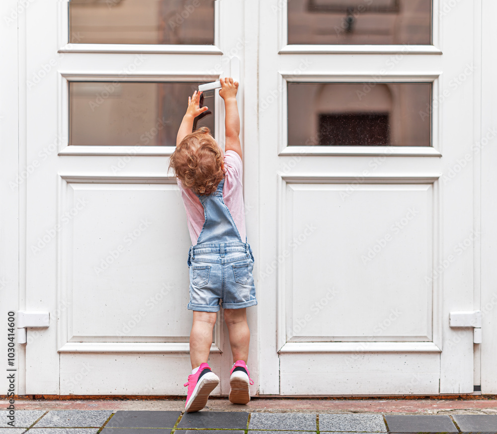 The child tries to open the door. The child reaches for the doorknob on the street.