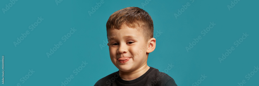 Sticking his tongue out, boy shows off his playful side against blue studio background. His expression full of character and youthful charm. Concept of facial-expressions, positive emotions. Ad Sticking his tongue out, boy shows off his playful side against blue studio background. His expression full of character and youthful charm. Concept of facial-expressions, positive emotions. Ad