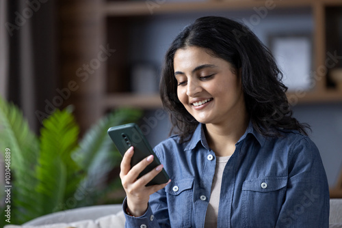 Photography Close-up photo of a young Indian woman in a denim shirt at home, sitting on a so