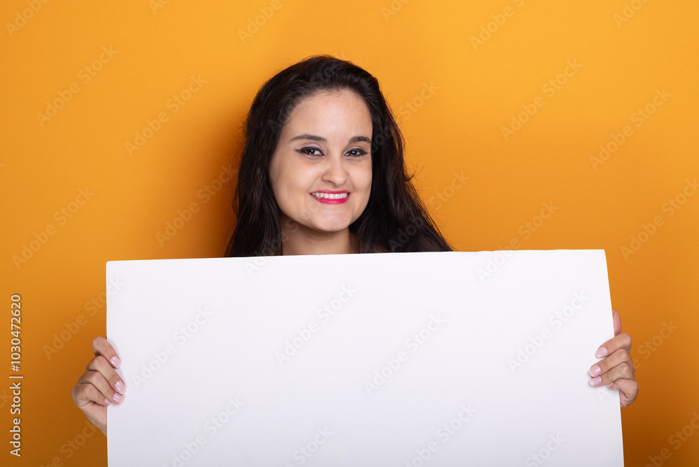 Young latin american woman holding blank banner with happy face, standing and smiling with confident smile, showing teeth, looking at camera. Young latin american woman holding blank banner with happy face, standing and smiling with confident smile, showing teeth, looking at camera.