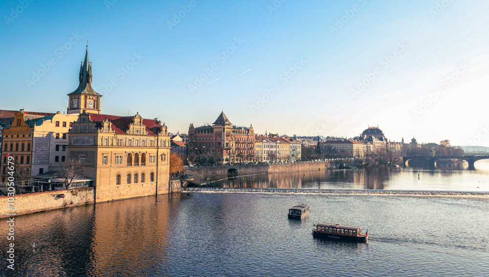 Fototapeta premium Sunrise over the Vltava River highlighting historic buildings and boat activity in Prague