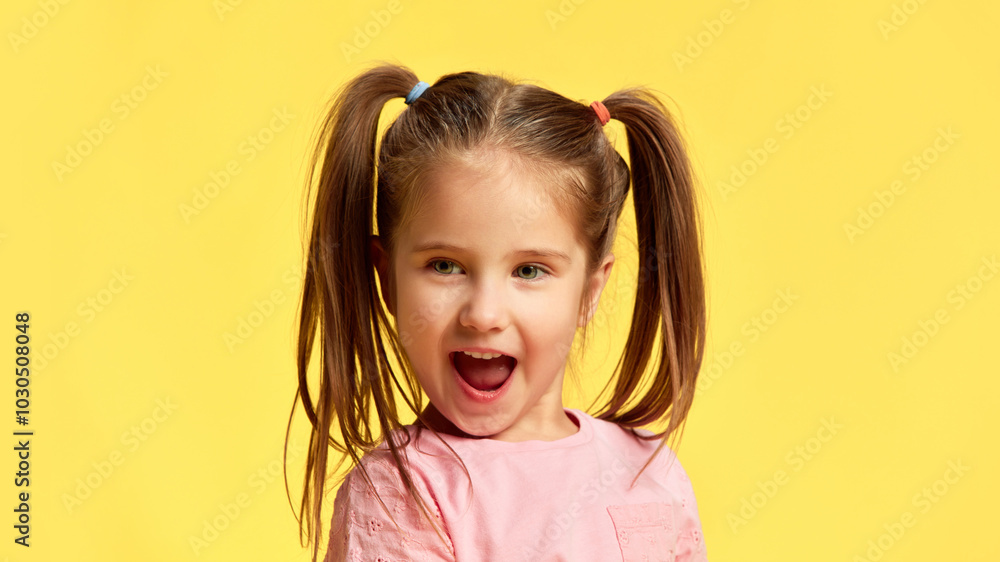 Little girl with funny pig-tails reacts with open mouth, showing surprise and excitement against sunny yellow background. Concept of facial-expressions, positive and negative emotions. Ad Little girl with funny pig-tails reacts with open mouth, showing surprise and excitement against sunny yellow background. Concept of facial-expressions, positive and negative emotions. Ad