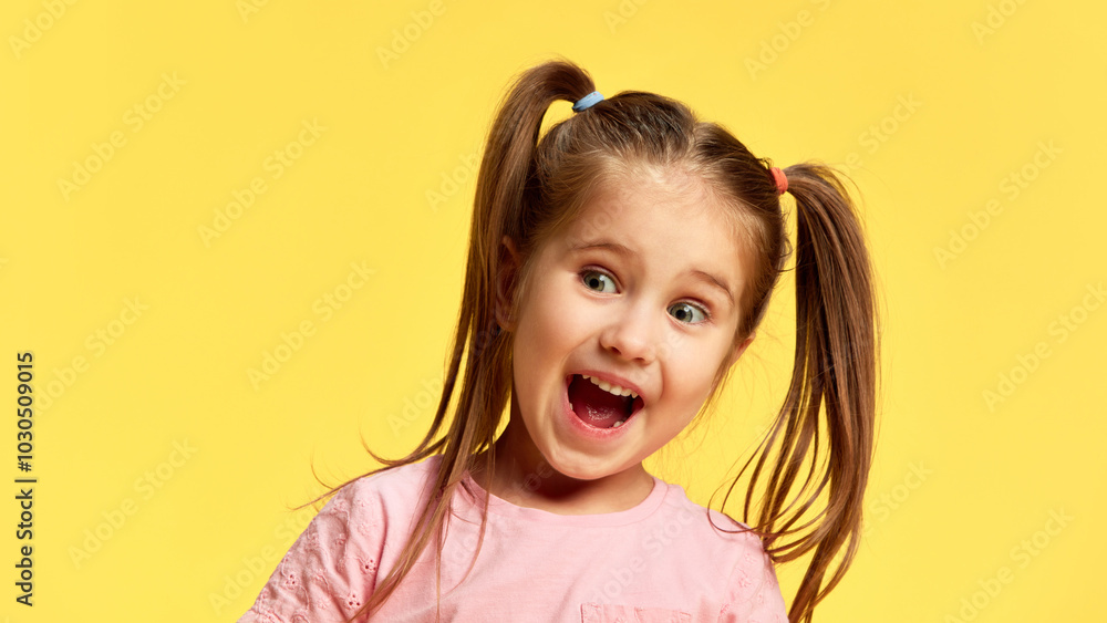 Little charming girl expresses wonder, eyes wide open and mouth slightly agape against sunny yellow background. Concept of facial-expressions, positive and negative emotions. Ad Little charming girl expresses wonder, eyes wide open and mouth slightly agape against sunny yellow background. Concept of facial-expressions, positive and negative emotions. Ad