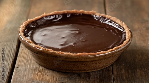 Chocolate ganache tart in a rustic ceramic dish, with a warm wooden background that makes the shiny, smooth surface stand out.