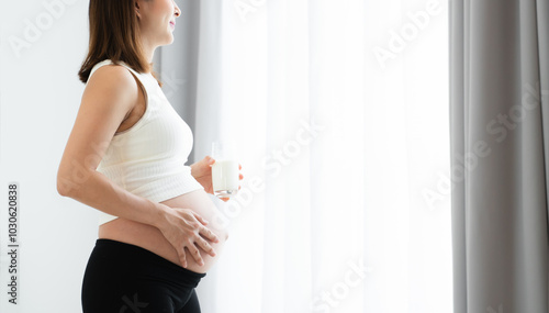 Side view of Pregnant Asian young woman standing and holding a glass of fresh milk near her belly with love and care at home. Pregnancy lifestyle. Copy space. Selective focus on hand touching belly Free Download Side view of Pregnant Asian young woman standing and holding a glass of fresh milk near her belly with love and care at home. Pregnancy lifestyle. Copy space. Selective focus on hand touching belly - GFXLoad