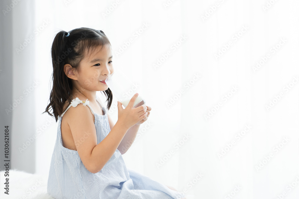 Asian little cute kid with mustache of milk on lips, holding a glass of milk, sitting at home. Young preschool child girl smiling, enjoy drinking milk for good health for breakfast in morning Asian little cute kid with mustache of milk on lips, holding a glass of milk, sitting at home. Young preschool child girl smiling, enjoy drinking milk for good health for breakfast in morning