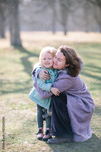 Young beautiful mother and an adorable blond little daughter are hugging and in a park in spring, happy family