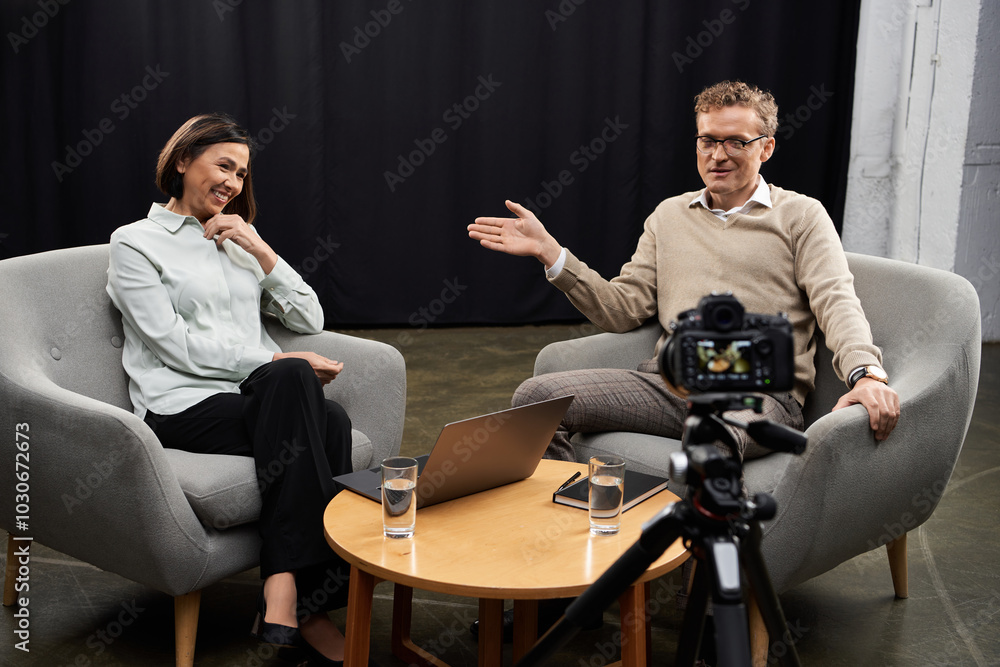 A middle aged female journalist engages with a male expert in a professional interview atmosphere. A middle aged female journalist engages with a male expert in a professional interview atmosphere.