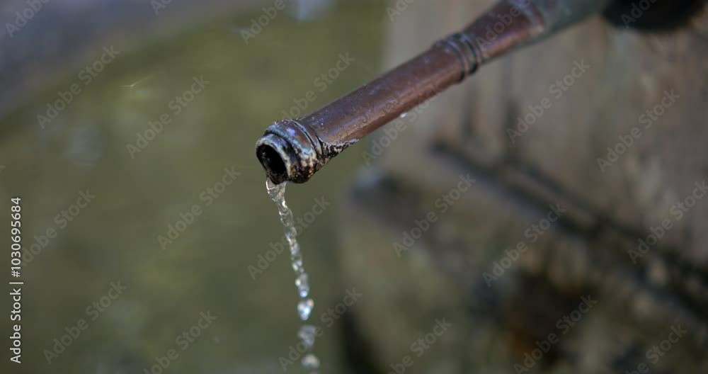 Close-up of an old metal faucet dripping water into a fountain, slow motion at 800 fps, rustic and aged appearance, peaceful water flow in a public outdoor setting Close-up of an old metal faucet dripping water into a fountain, slow motion at 800 fps, rustic and aged appearance, peaceful water flow in a public outdoor setting