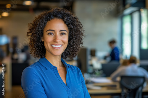Happy young Hispanic American woman in a blue blouse standing in the office smiling.
