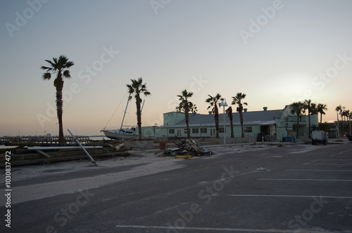 Parking  Lot Trash Beach damaged piled storm surge  after hurricanes Helene and Milton at Gulfport Beach in Florida. Debris, sand, orange detour sign and temporary fence.  Late afternoon Sun