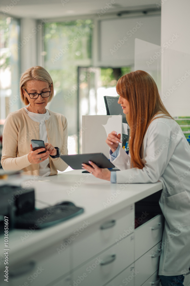 Pharmacist with tablet leaning on counter and selling drugs to old woman Pharmacist with tablet leaning on counter and selling drugs to old woman